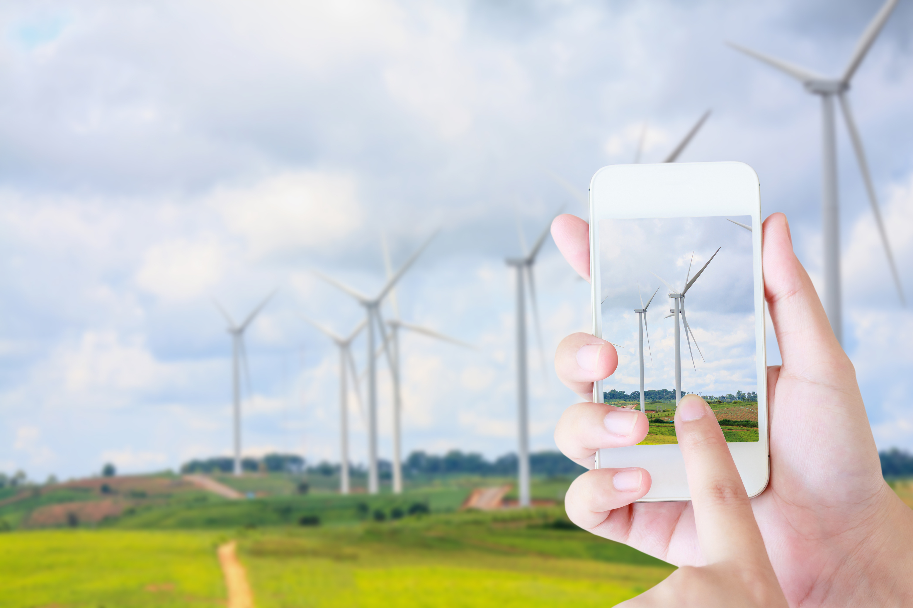Hands holding a cellphone taking a photo of wind turbines.